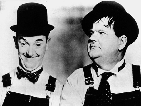 Black and white photograph of performers Stan Laurel and Oliver Hardy wearing top hats and overalls.